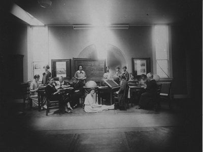 Margaret Harwood sits on the floor for this posed tableau taken on May 19, 1925. Harvia Wilson is at far left, sharing a table with Annie Cannon (too busy to look up) and Antonia Maury (left foreground). The woman at the drafting table is Cecilia Payne.